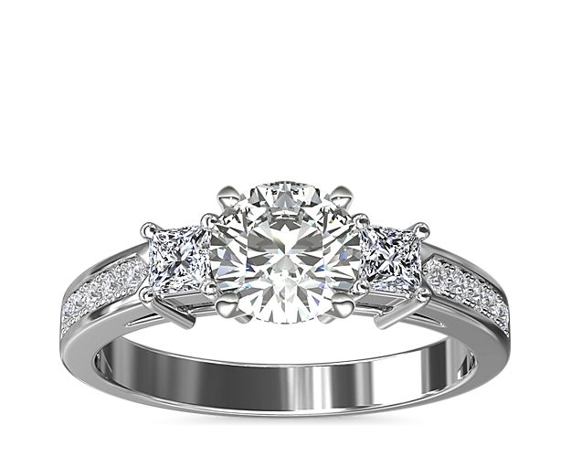 An elegantly designed 14k white gold petite diamond engagement ring featuring two princess-cut side diamonds and 10 round pavé-set diamonds flanking the center stone of your choice. The sidestones on the setting equal 1/3-carat total weight.