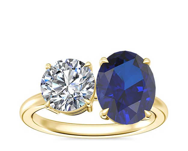 A brilliant oval-cut sapphire nestles next to a hoice of round, princess, pear, asscher, emerald-cut, radiant, cushion, marquise, heart, or oval-cut stone in this gorgeous two-stone engagement ring. It features 18k yellow gold design that beautifully complements the hue of the sapphire.