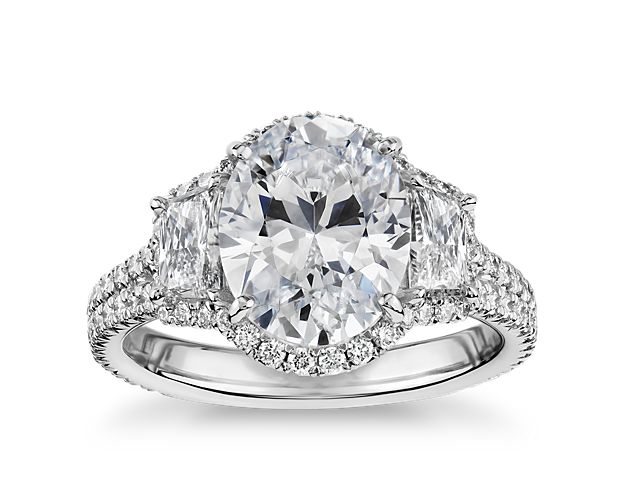 The oval-shaped center stone of your choice sits at the center of this breathtaking platinum ring and is flanked by dazzling trapezoid diamonds and surrounded by a brilliant pavé halo. For center stones 1.5  to 3 carats. Centers stones to accommodate centers down to 0.5 carats, use stock # 68096.